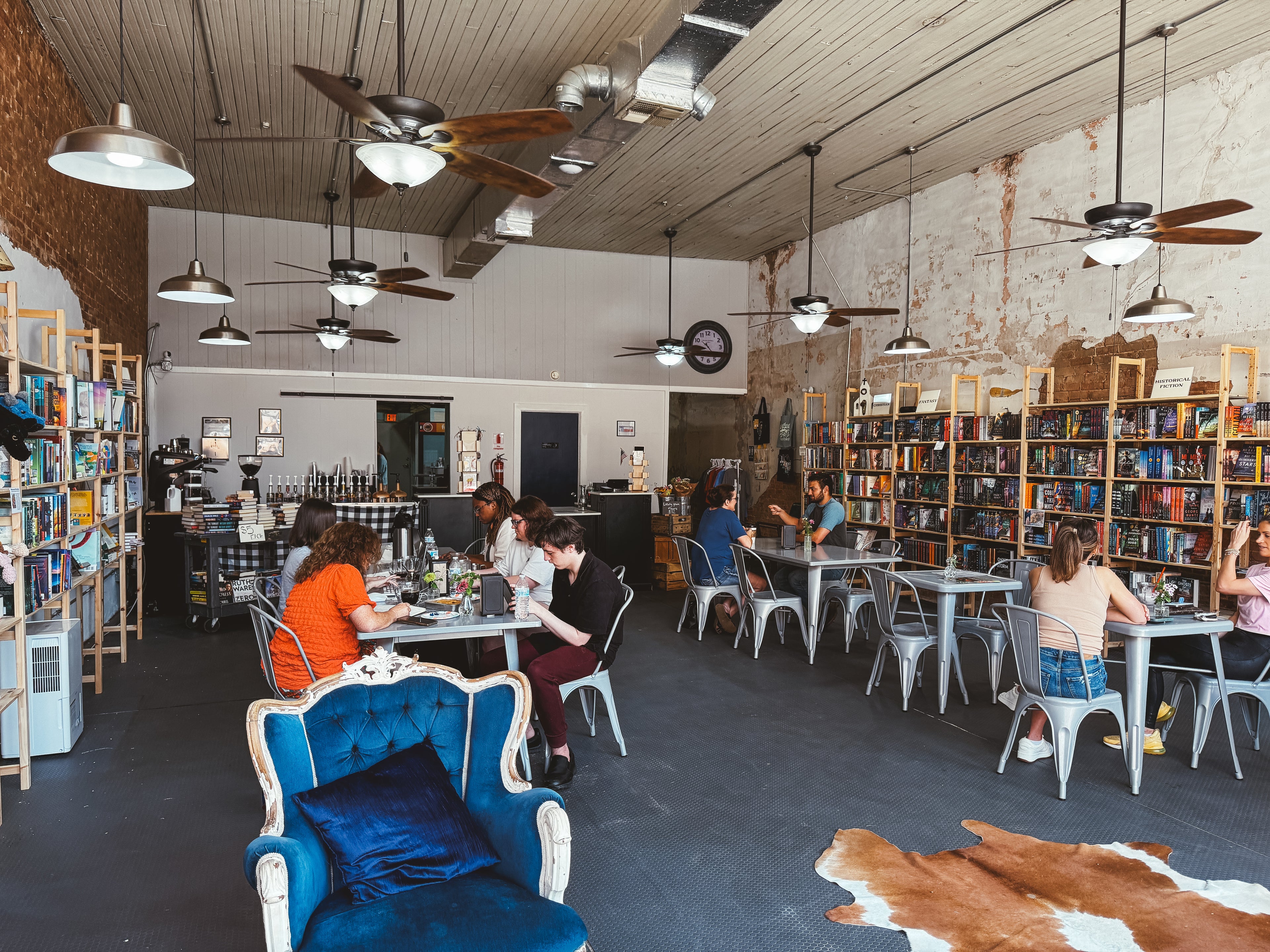 Indoors of a cafe with people sitting at tables, books on shelves, and a blue chair.
